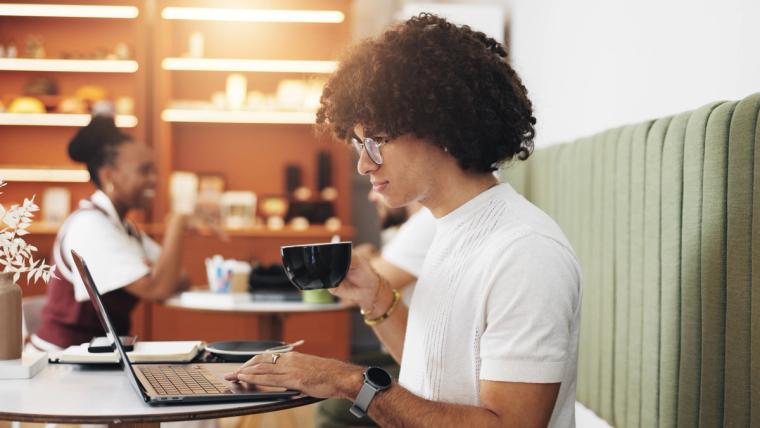 J2 Visa Holder Working Remotely With Ead Work Permit | Immiva Young professional with curly hair working on laptop at a coffee shop, representing J2 visa holders who can work freely in the U.S. after obtaining their EAD work permit