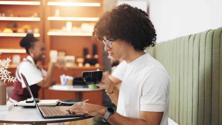 Young professional with curly hair working on laptop at a coffee shop, representing J2 visa holders who can work freely in the U.S. after obtaining their EAD work permit