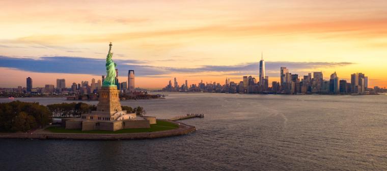 Statue of Liberty - Symbol of U.S. Citizenship and Immigration | Immiva The Statue of Liberty at sunset overlooking New York Harbor with the Manhattan skyline in the background, representing the promise of American citizenship for immigrants pursuing naturalization.
