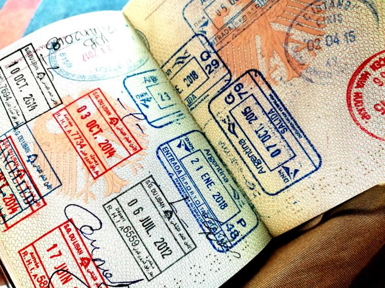 Passport with visa stamps | Immiva An open passport showing multiple pages filled with colorful entry and exit stamps from various countries