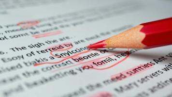 Red pencil marking spelling and grammar errors on printed text, representing preparation for the N-400 naturalization English reading and writing test