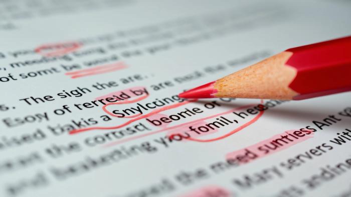Red pencil marking spelling and grammar errors on printed text, representing preparation for the N-400 naturalization English reading and writing test