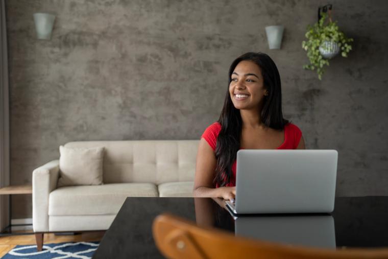 Young woman working from home on a laptop with notebooks on her desk