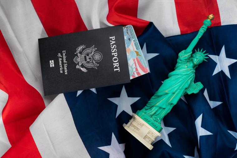 Simplified Immigration with Immiva: Passport, Green Card, and the American Dream | Immiva alt United States passport with a green card partially visible, next to a Statue of Liberty figure, placed on an American flag. Immiva provides efficient immigration solutions to help individuals achieve their American dream.
