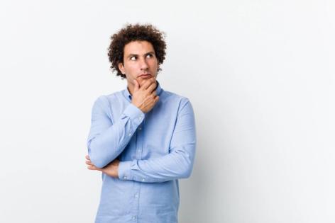 Thoughtful young man wearing a blue shirt looking sideways with a doubtful expression, illustrating the decision to file N-400 while I-751 is still pending