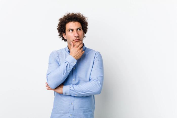 Man Thinking About N-400 Filing While I-751 Pending | Immiva Thoughtful young man wearing a blue shirt looking sideways with a doubtful expression, illustrating the decision to file N-400 while I-751 is still pending