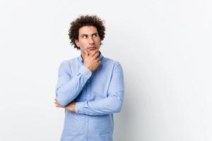 Thoughtful young man wearing a blue shirt looking sideways with a doubtful expression, illustrating the decision to file N-400 while I-751 is still pending