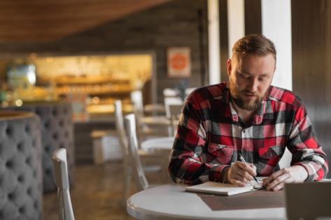Man in a cafe writing an invitation letter for a US B1 travel visa applicant, preparing a formal document for a visa application process