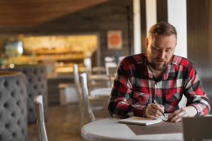 Man Writing an Invitation Letter for US B1 Travel Visa Applicant | Immiva Man in a cafe writing an invitation letter for a US B1 travel visa applicant, preparing a formal document for a visa application process