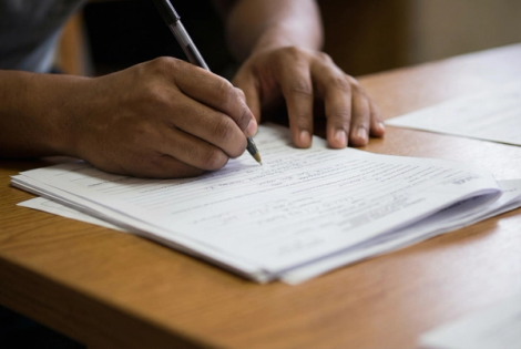 Person filling out a paper form by hand with a pen on a wooden desk, representing the DIY approach to completing immigration paperwork