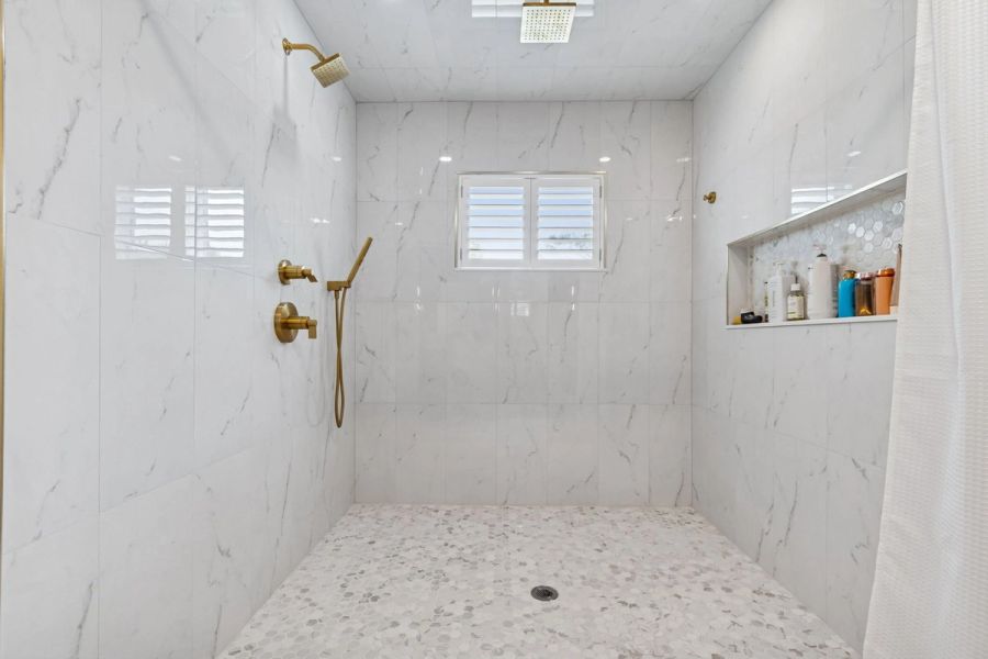 Interior primary bath walk in shower marble tile gold fixtures rain head — New home construction, Longboat Key