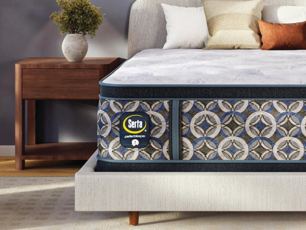 Hybrid pillow top mattress made up with bedding beside a nightstand
