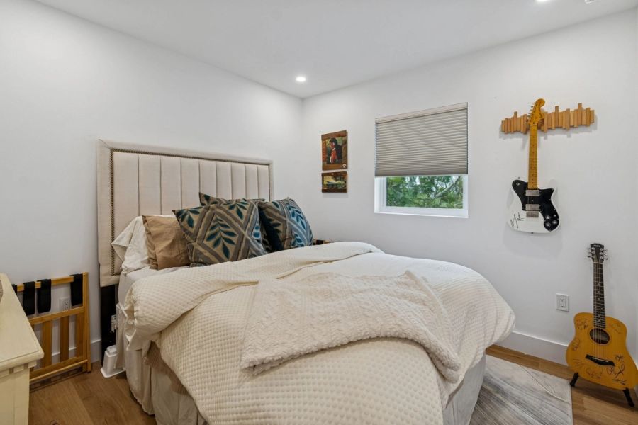 Interior guest bedroom upholstered headboard guitar wall art wood floors — New home construction, Longboat Key