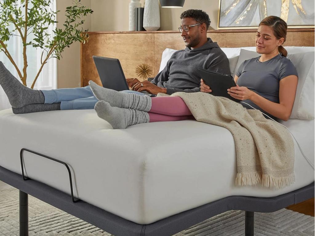 Couple sitting up in bed with a laptop and a tablet on the Gold base