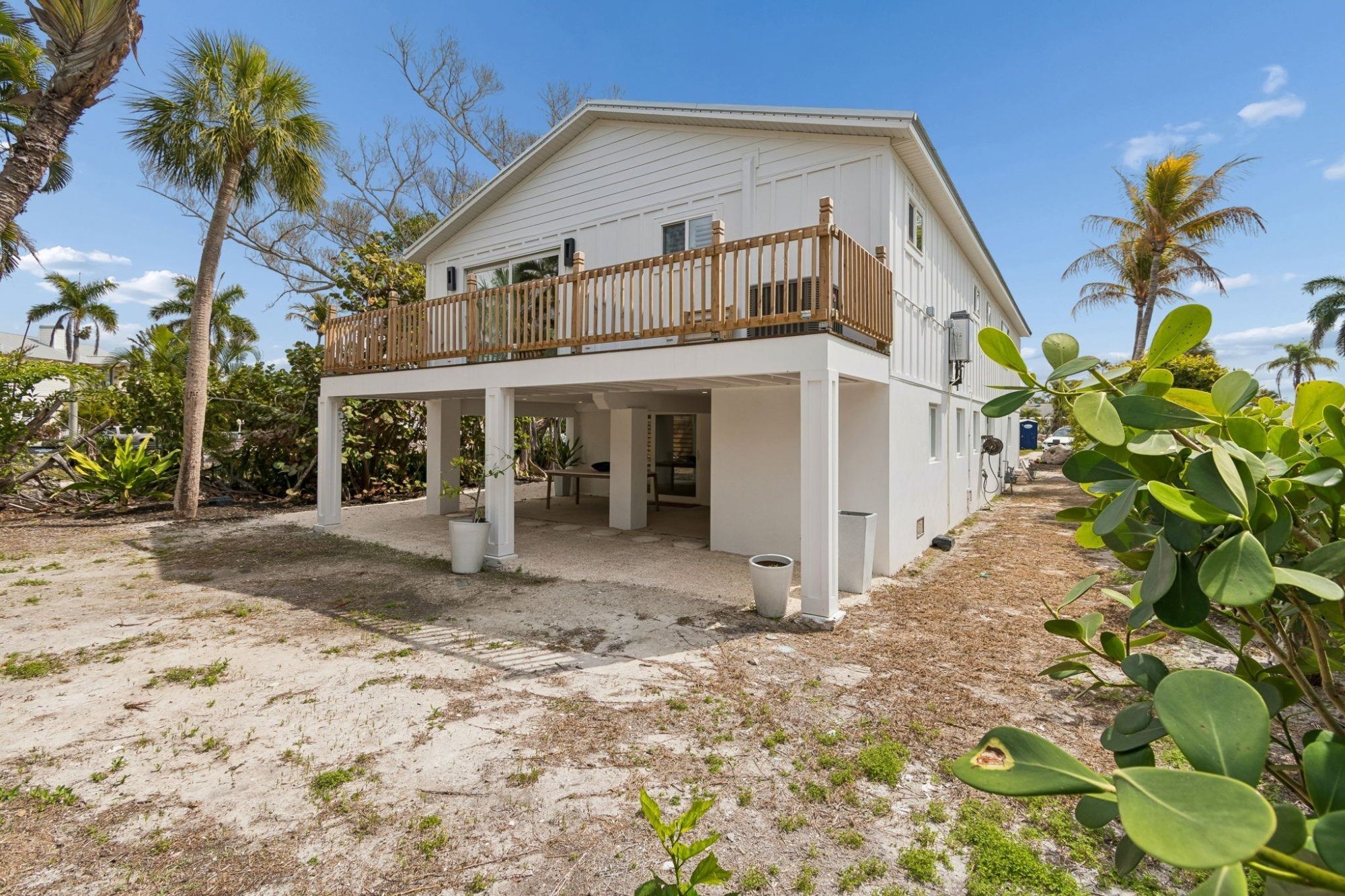 Coastal home rear exterior elevated pilings wood deck railing tropical yard — New home construction, Longboat Key