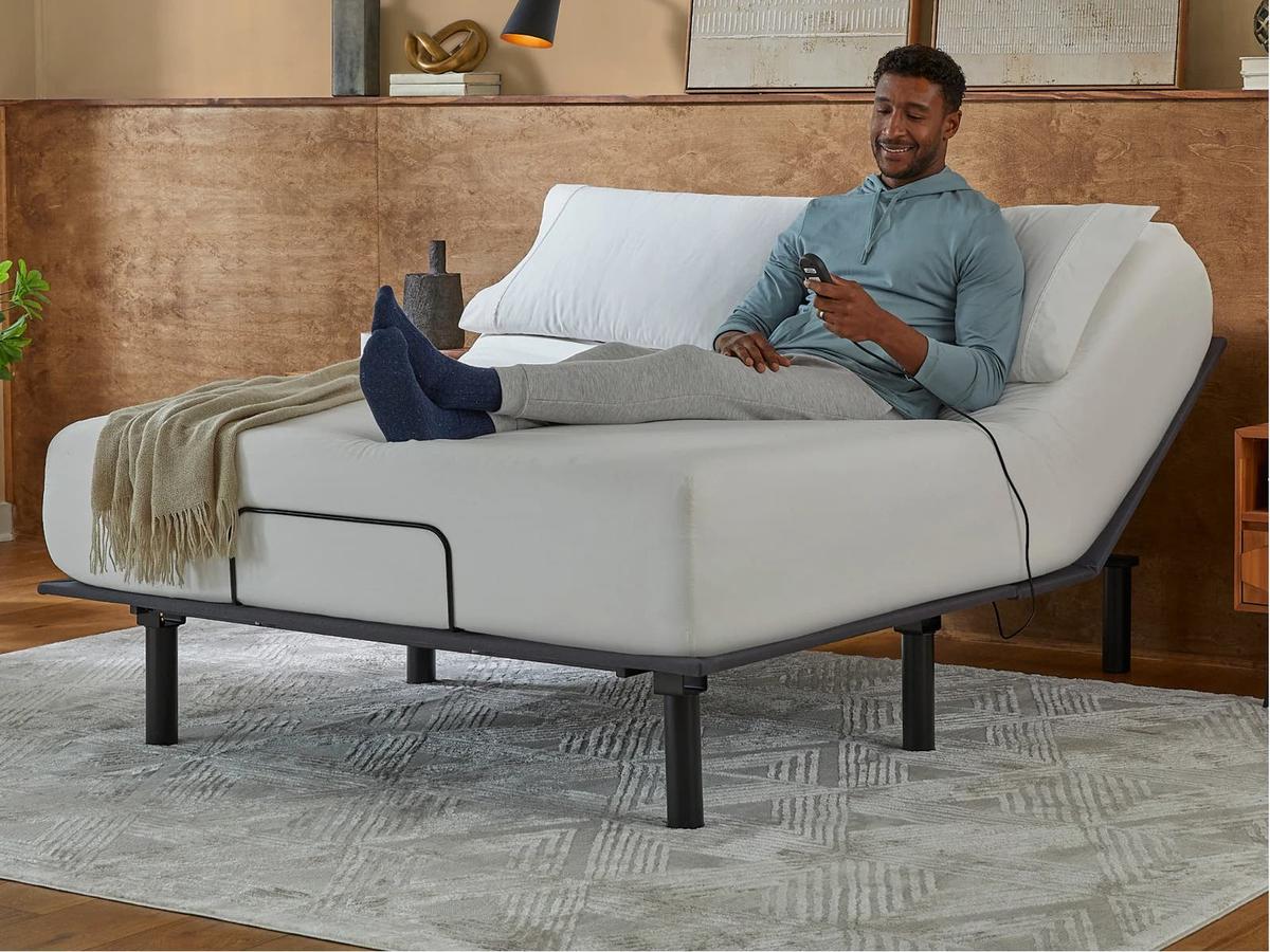 Man reclining on a bed with the head raised by the Bronze base, holding the remote