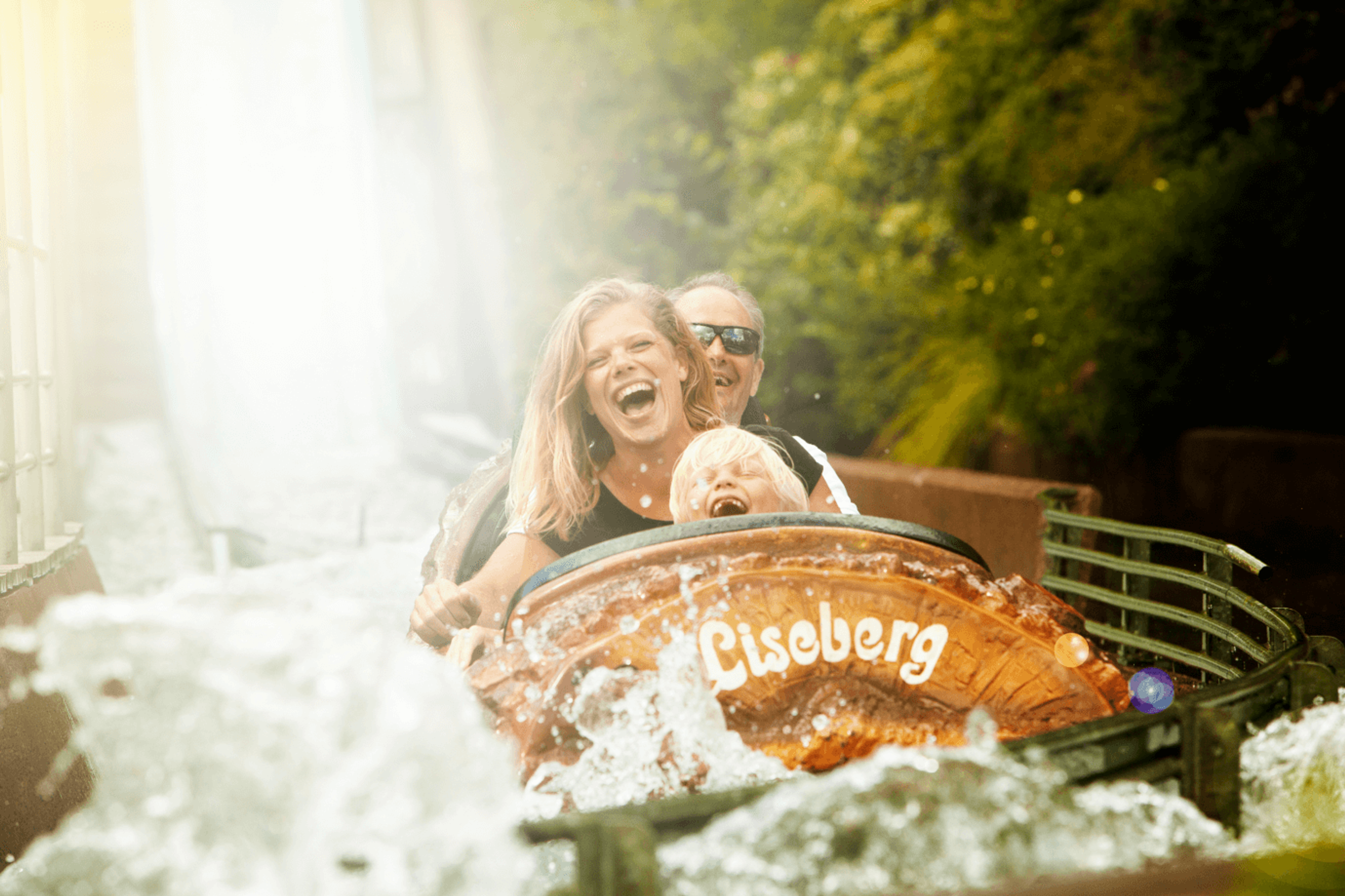 A photo showing two people on a ride crashing through water. The people are smiling and excited.