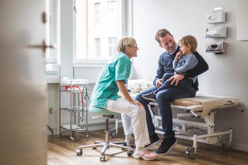 A doctor is talking to a parent and a child. The image is bright, the doctor in scrubs.
