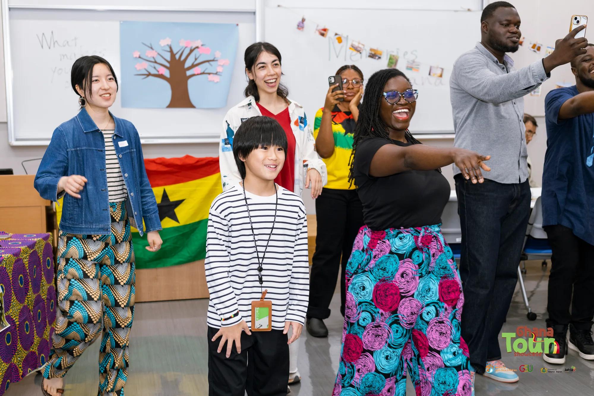 Child and guests dance in front of the Ghana flag, laughing together