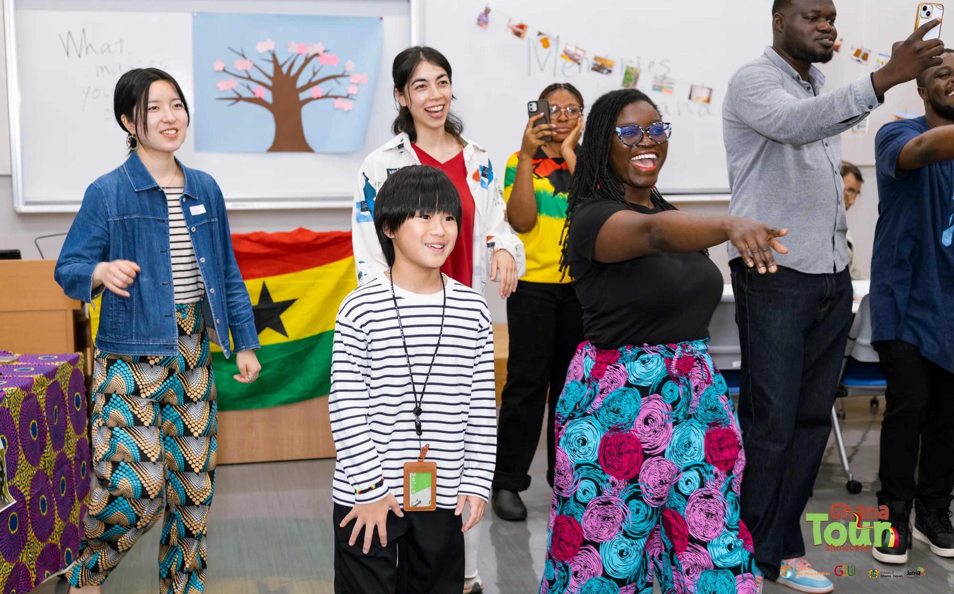 Child and guests dance in front of the Ghana flag, laughing together