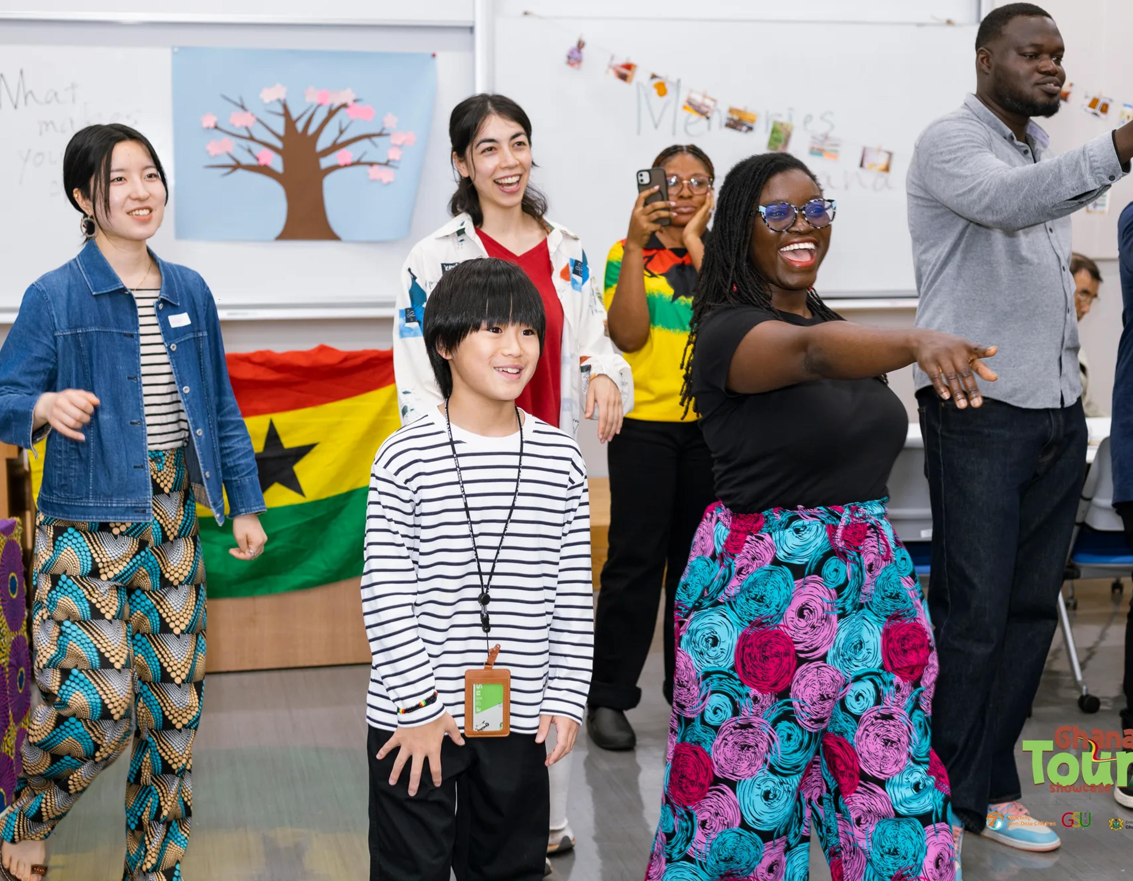 Child and guests dance in front of the Ghana flag, laughing together