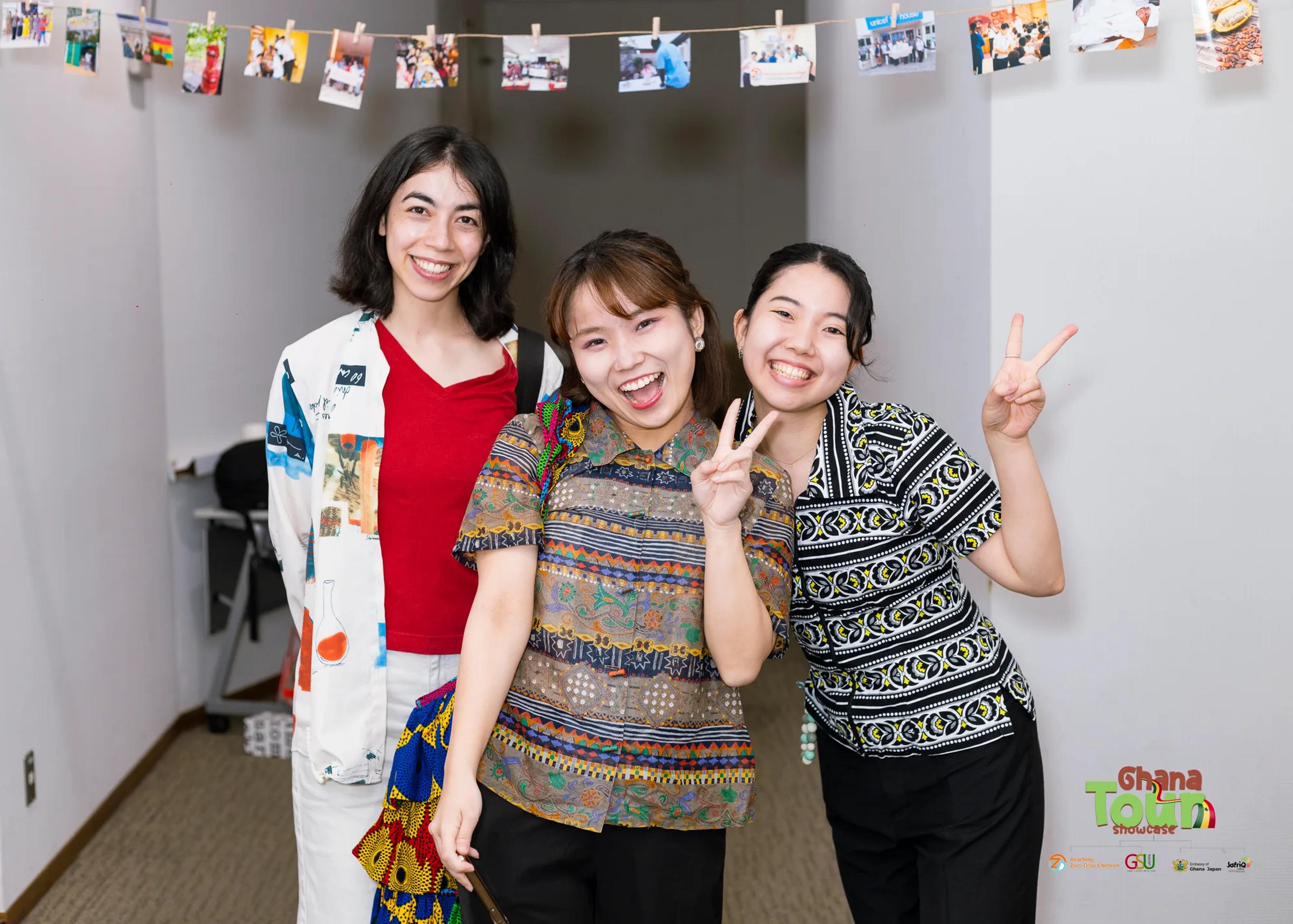 Three cheerful young women pose together under a line of hanging photos