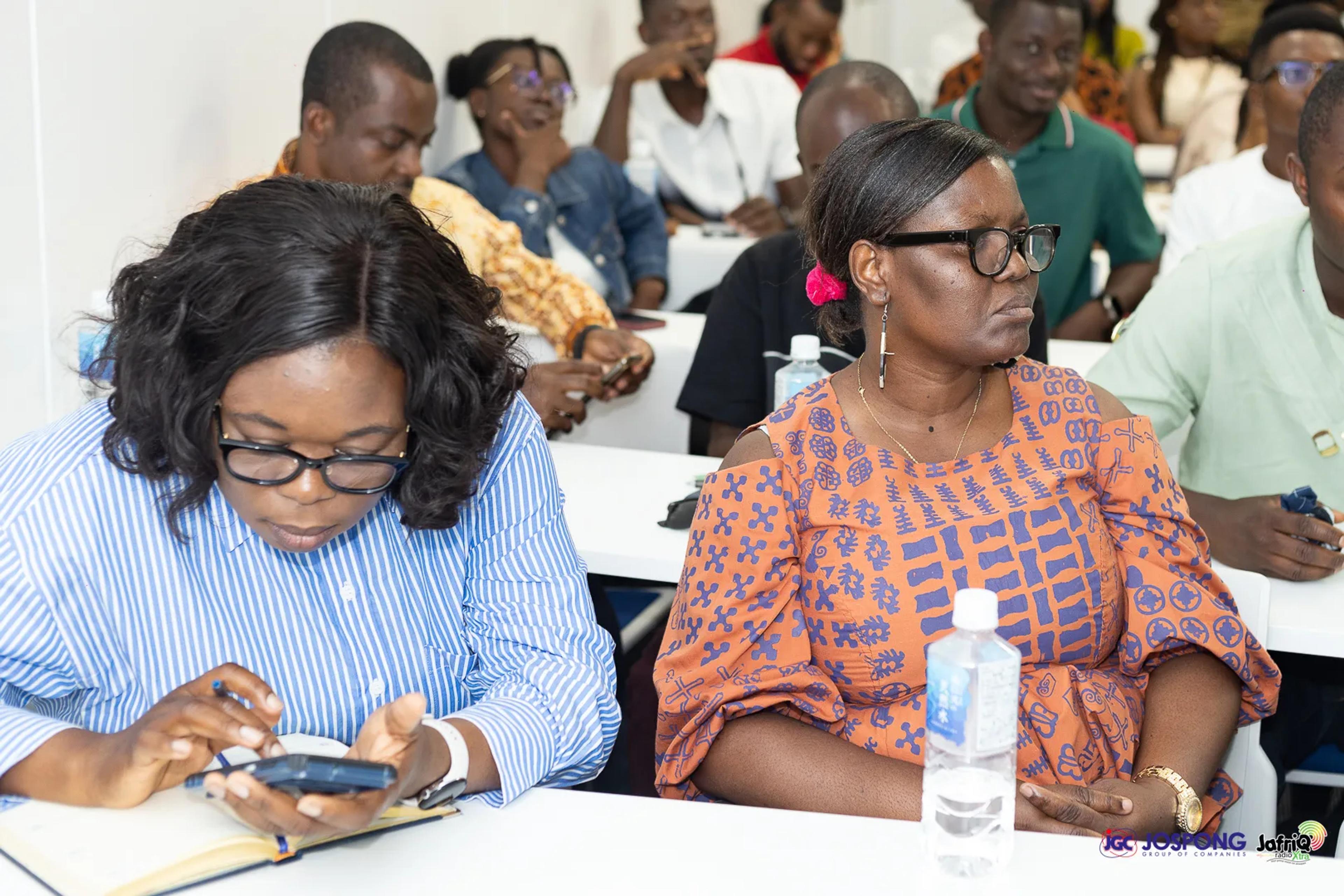Two attendees seated at a table, one checking her phone