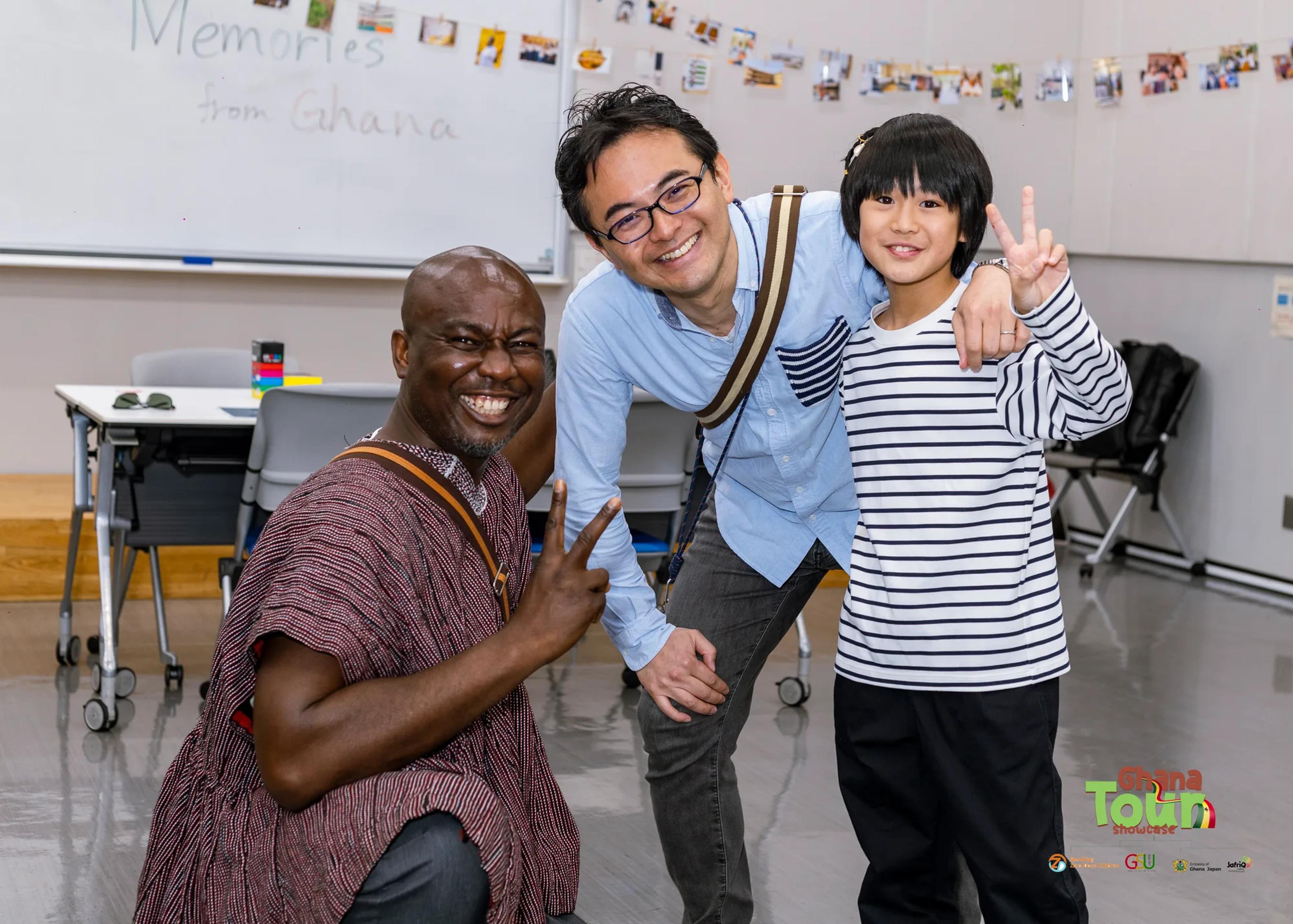 Ghanaian guest in a smock poses with a smiling father and son