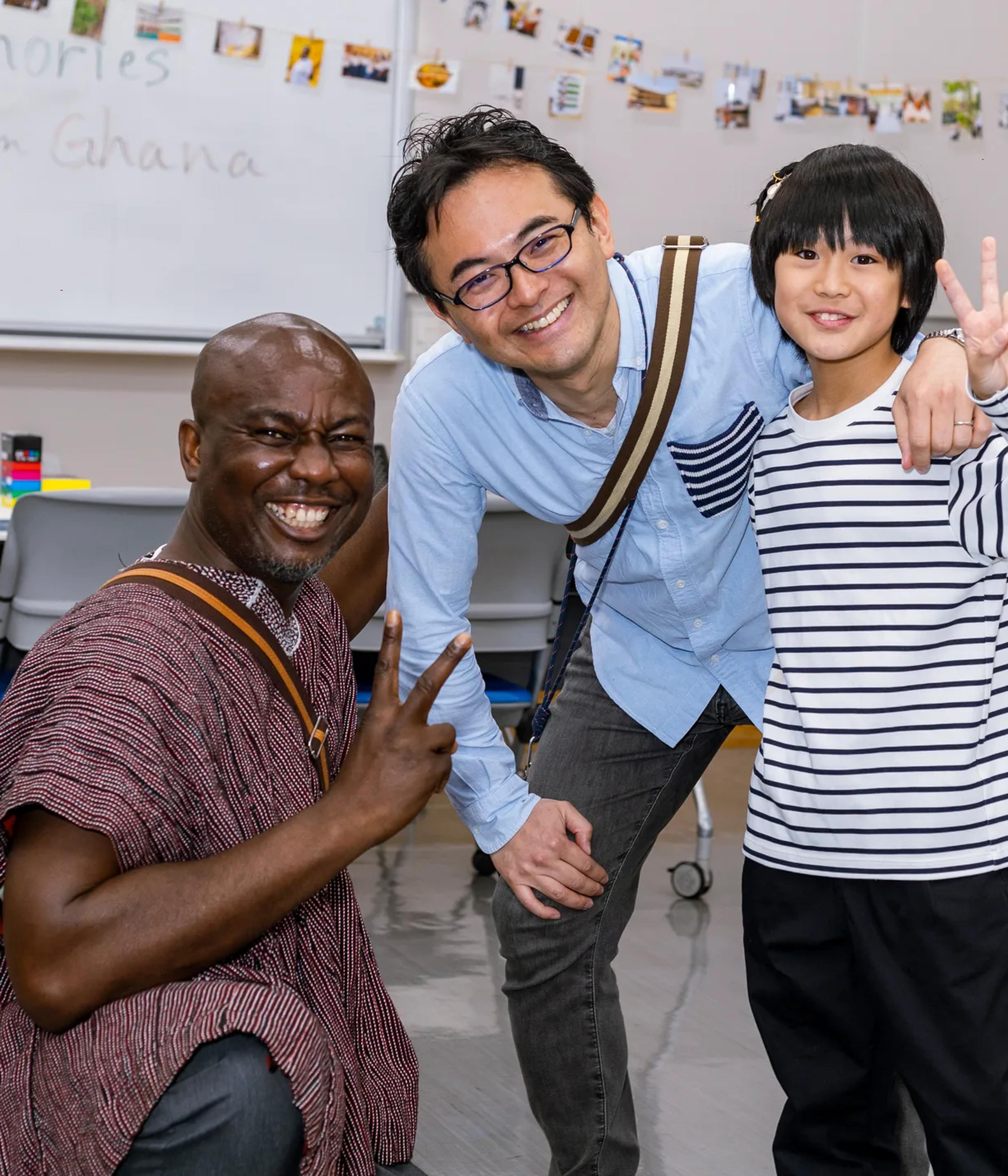Ghanaian guest in a smock poses with a smiling father and son