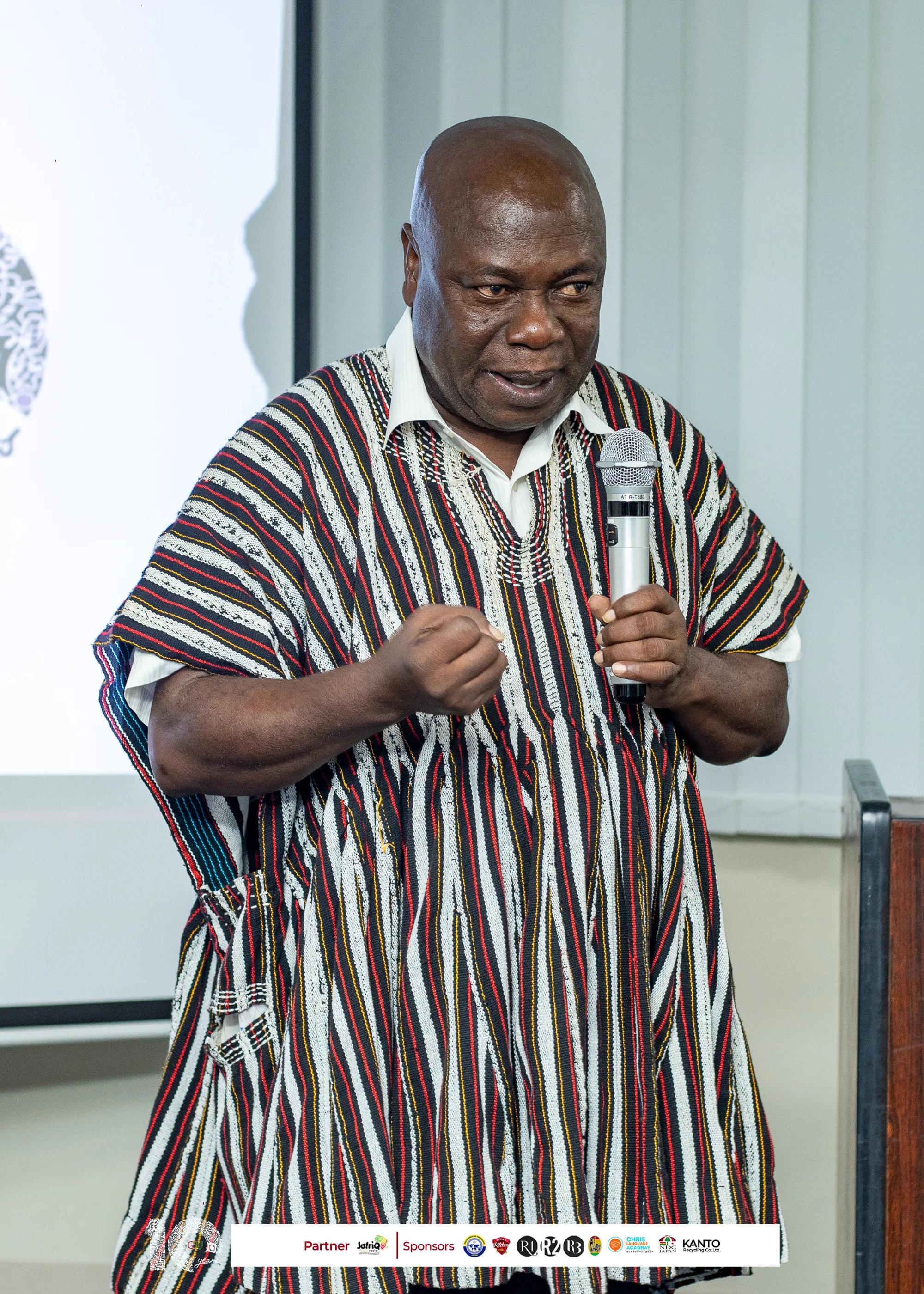 Guest speaker in a striped smock addresses the audience with a microphone