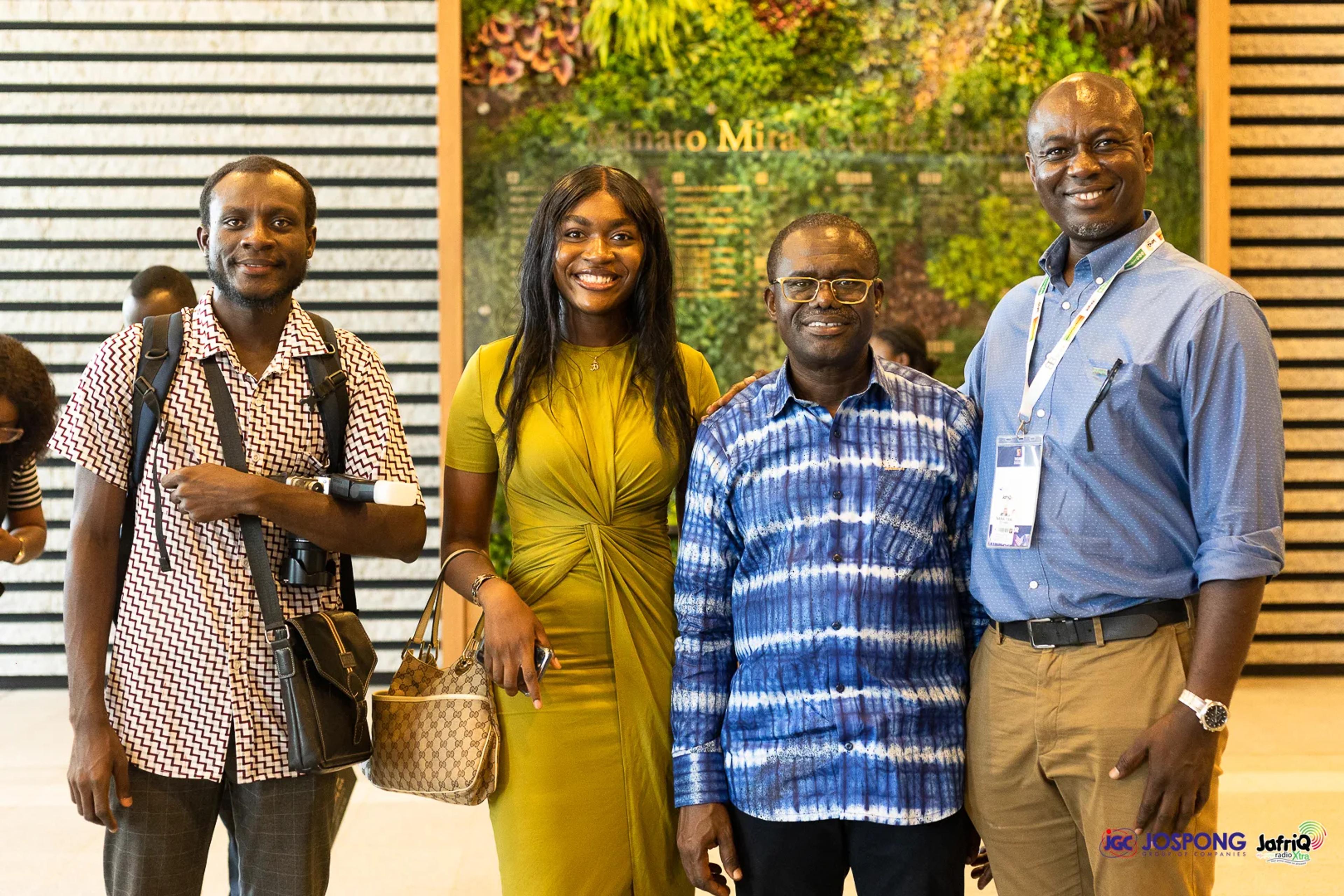 Four attendees pose together in front of the green wall