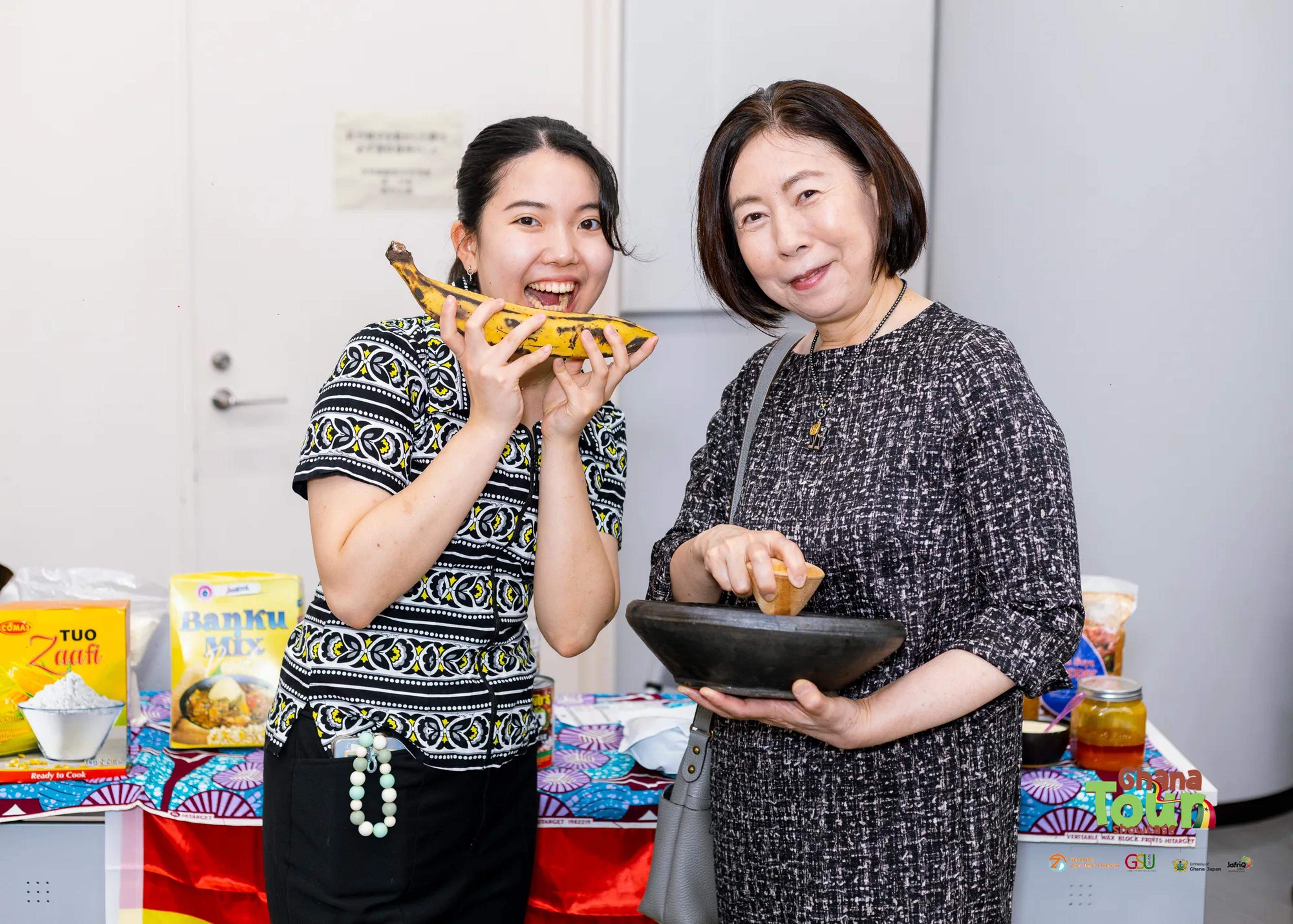 Two guests smile while tasting Ghanaian food at the food display