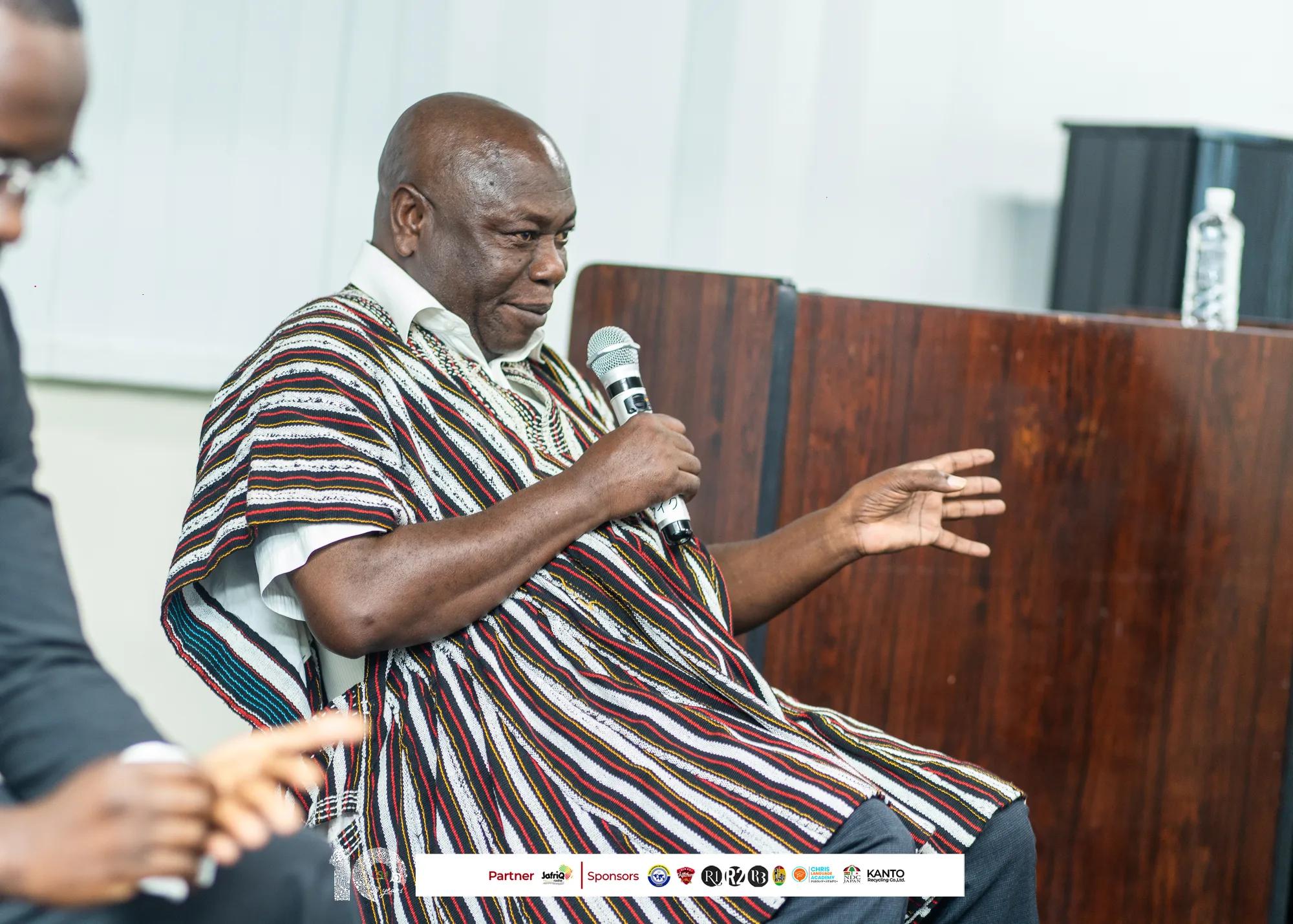 Seated speaker in a smock gestures while sharing his remarks