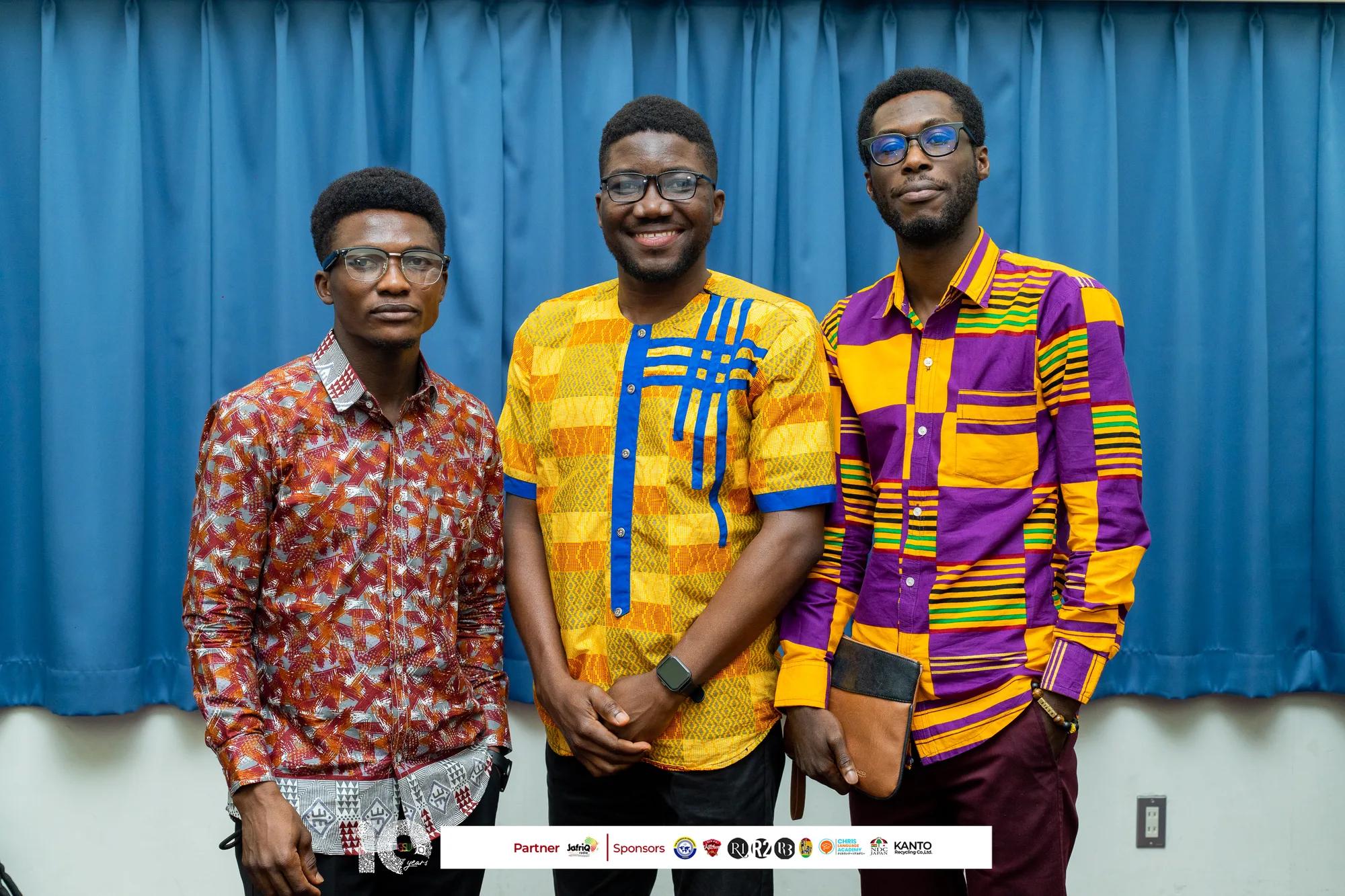 Three young members in colourful kente and print shirts smile together
