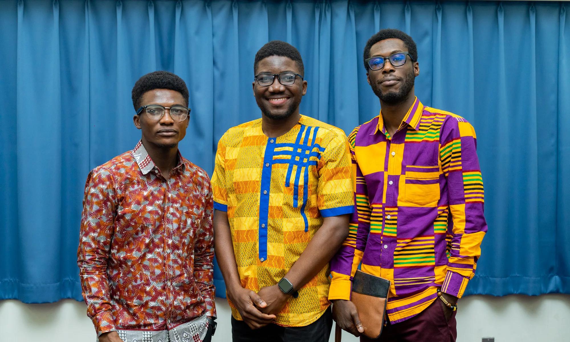 Three young members in colourful kente and print shirts smile together