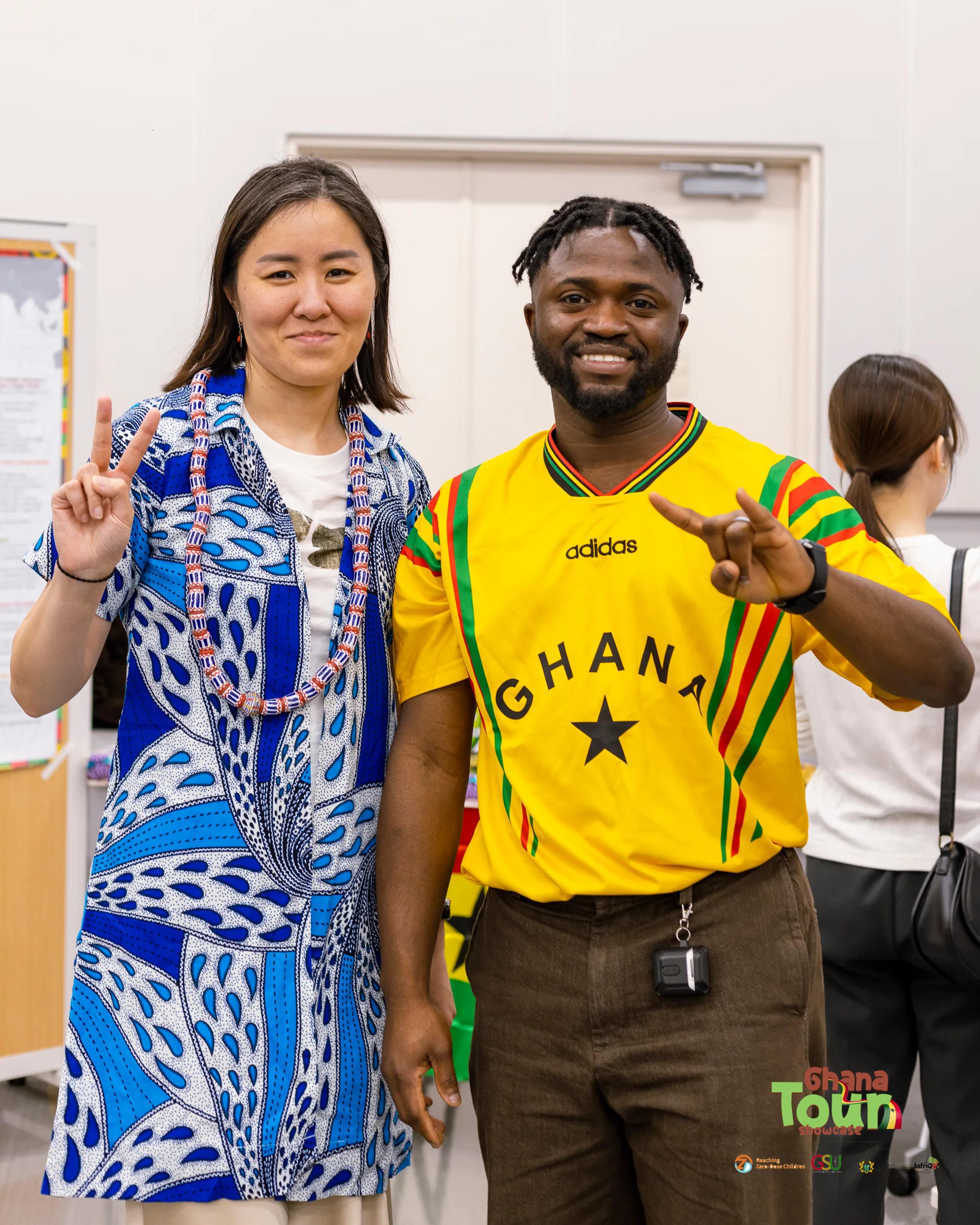 Guest in beads and blue print poses with a man in a Ghana jersey