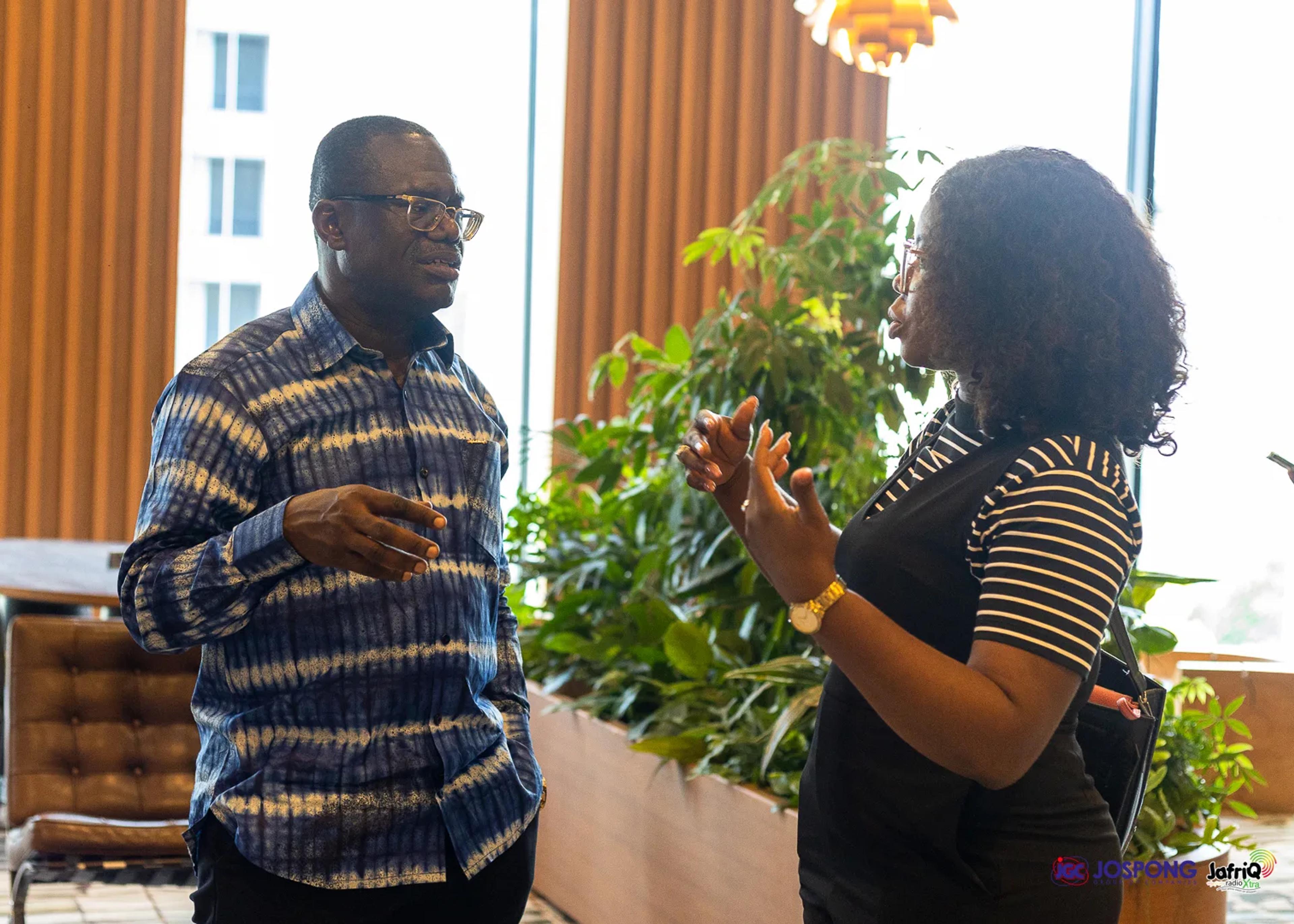 Guest and attendee chat beside large windows and indoor plants