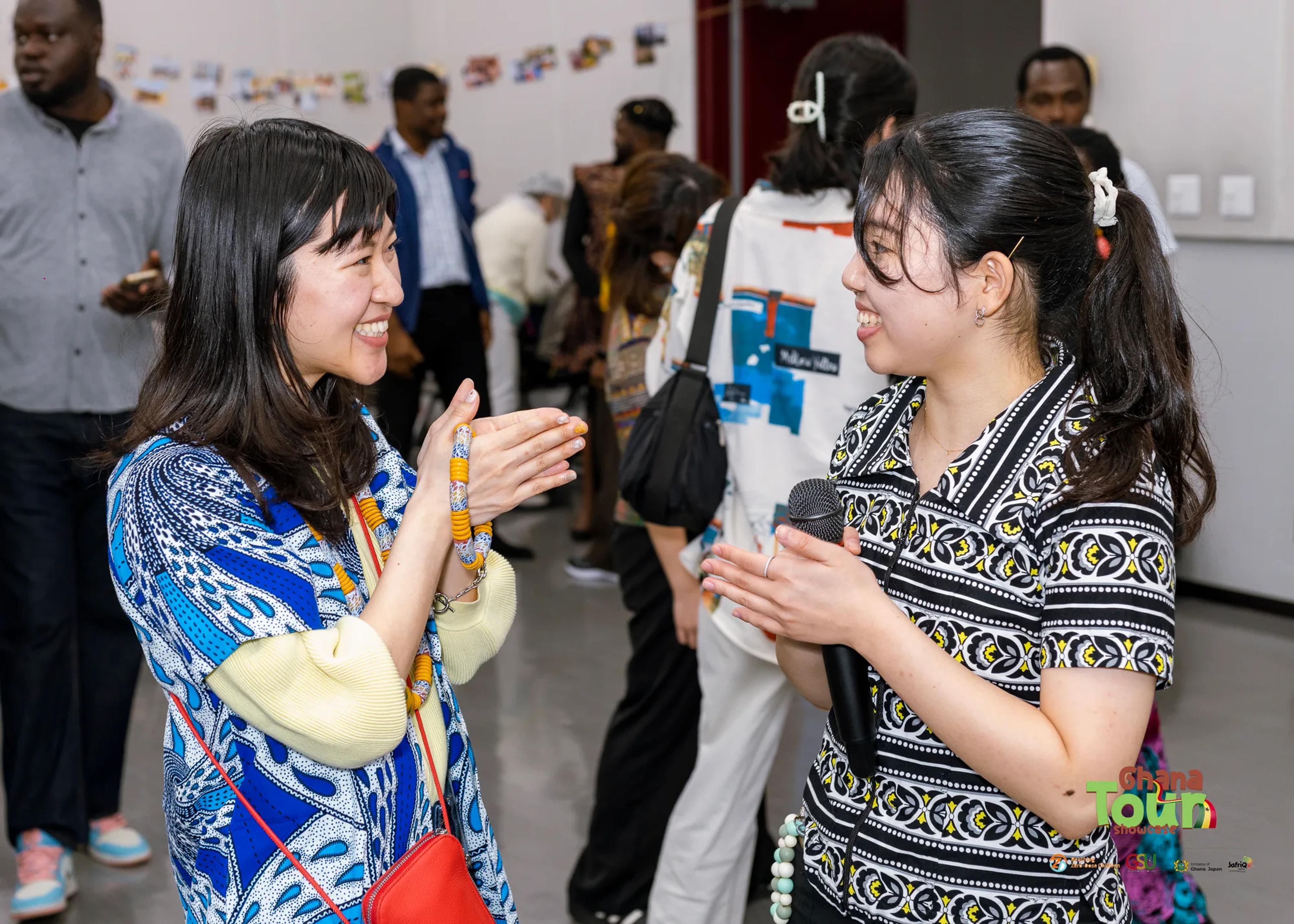 Two young women in African print chat and laugh during the expo