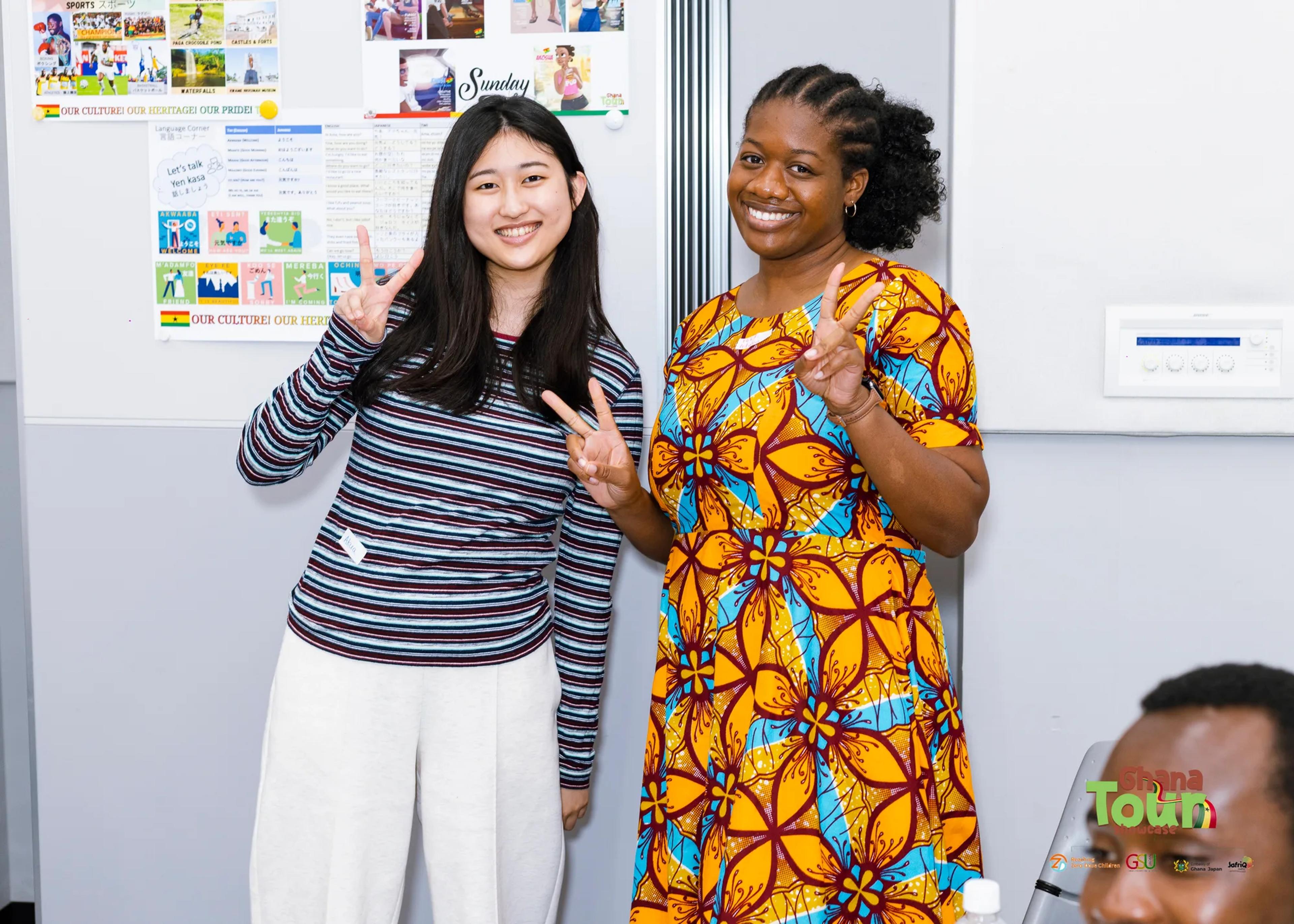 Two smiling friends, one in an African print dress, flash peace signs