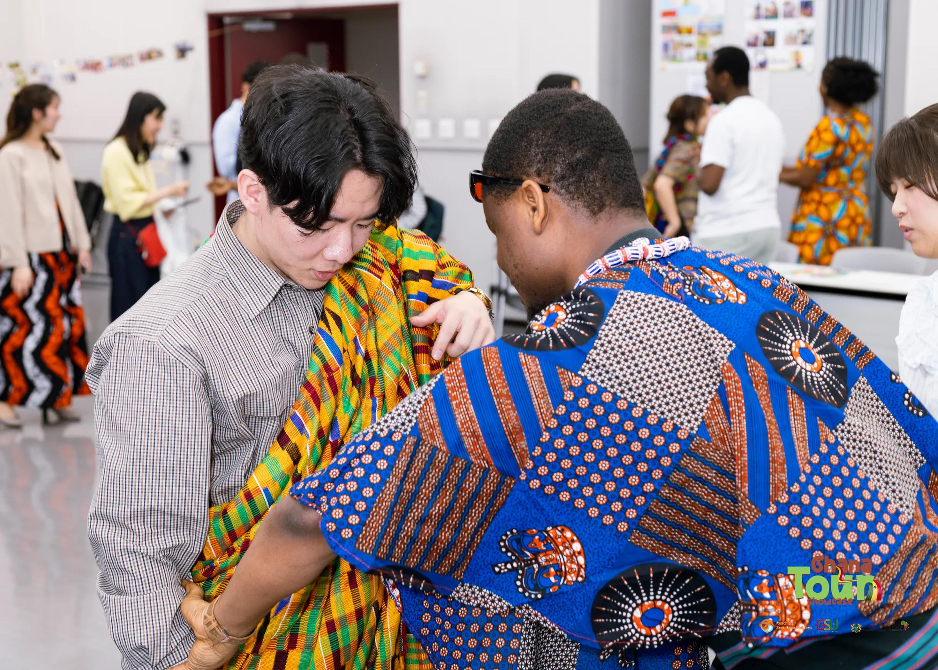 Visitor is draped in a kente cloth by a member in African print