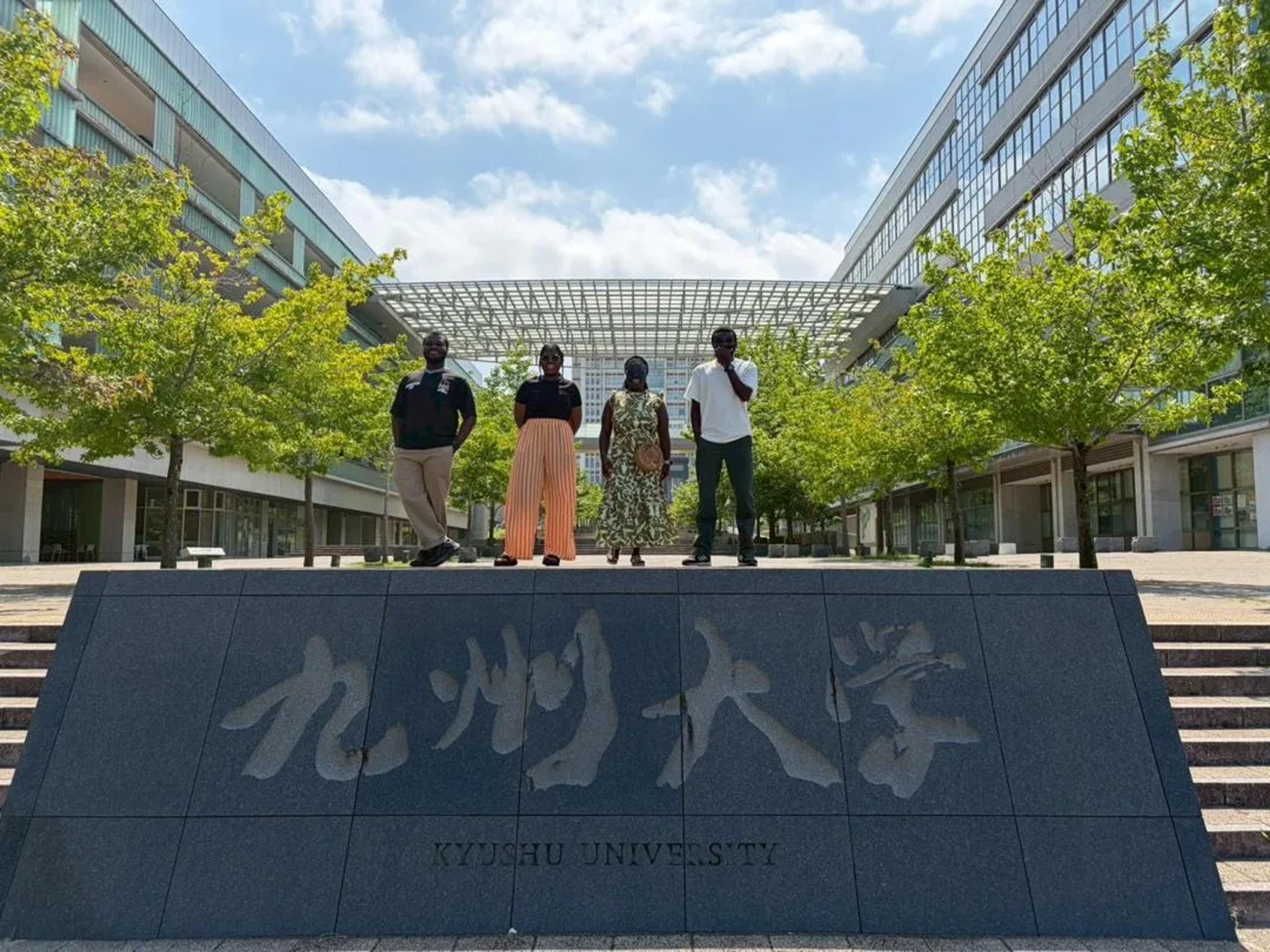 The team standing above the Kyushu University stone sign on the Ito campus