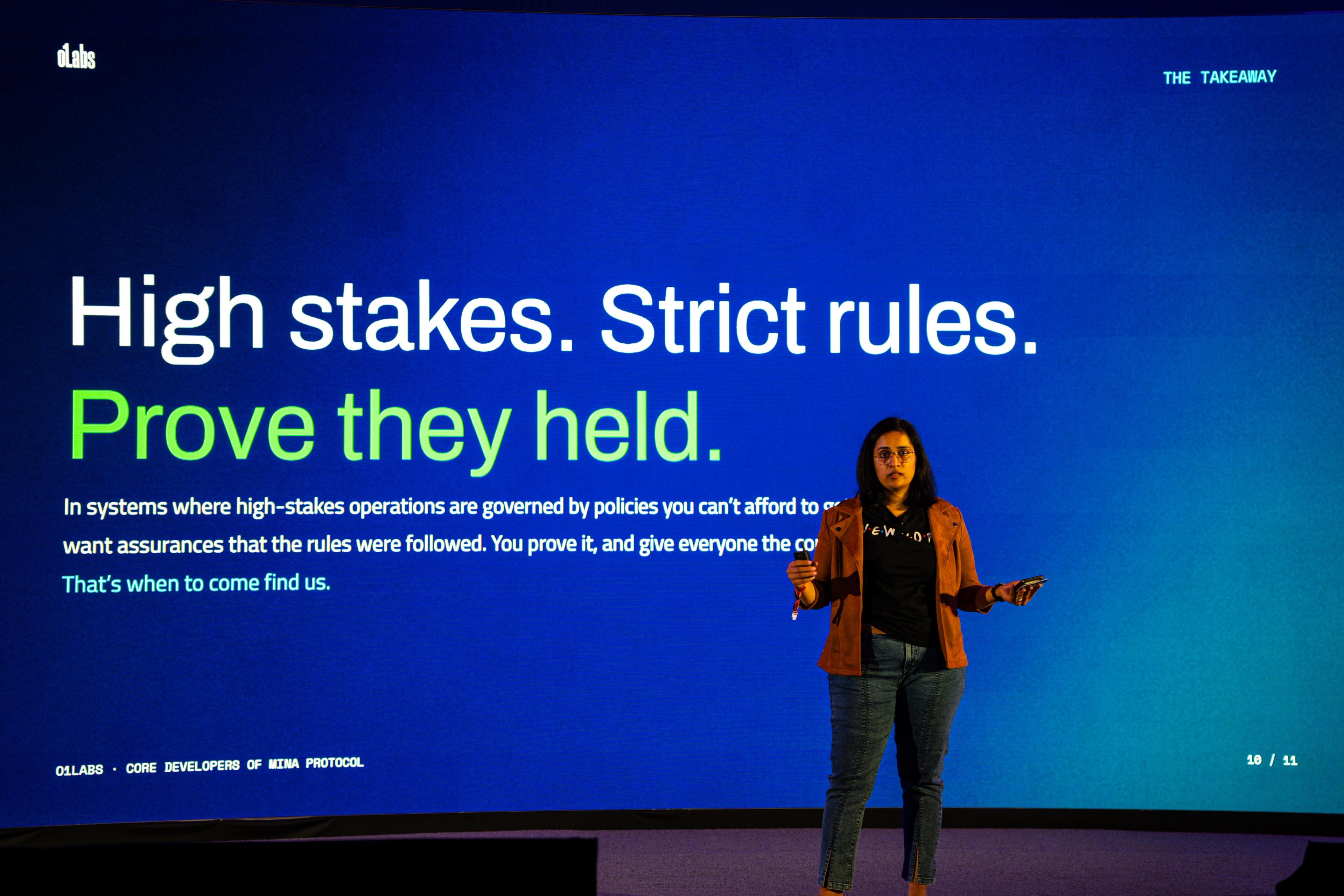 Deepthi Kumar on stage at EthConf, with a presentation slide reading "High stakes. Strict rules. Prove they held".
