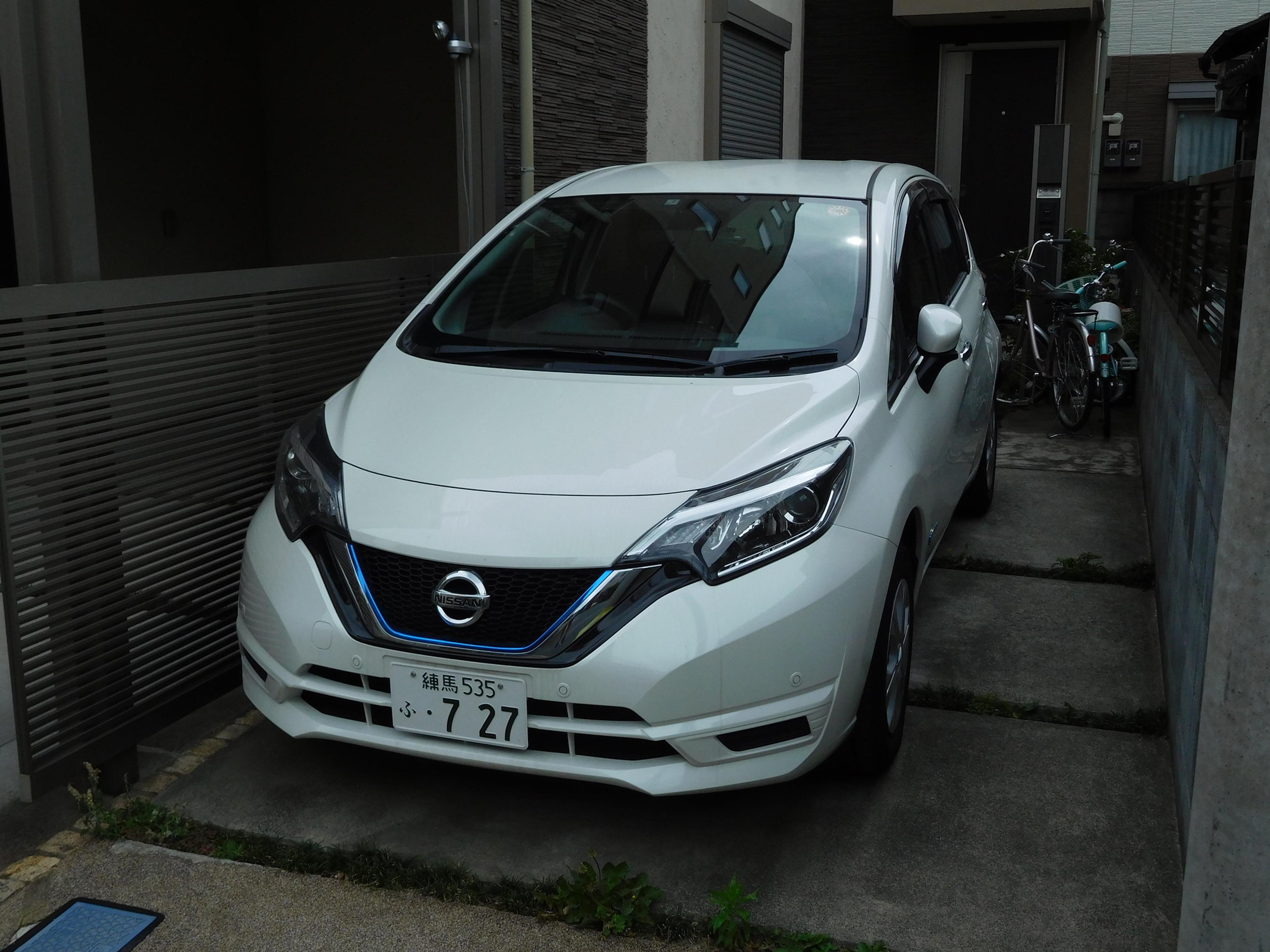 A white Nissan Note e-Power parked next to a home