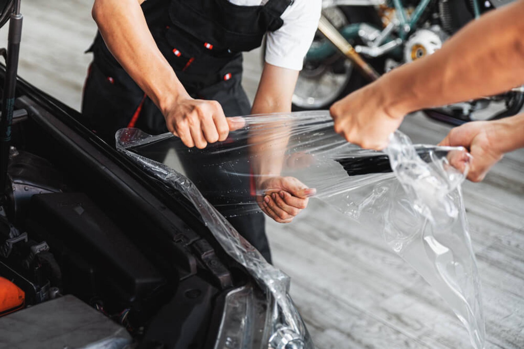 Two people by the car peeling off paint protection film