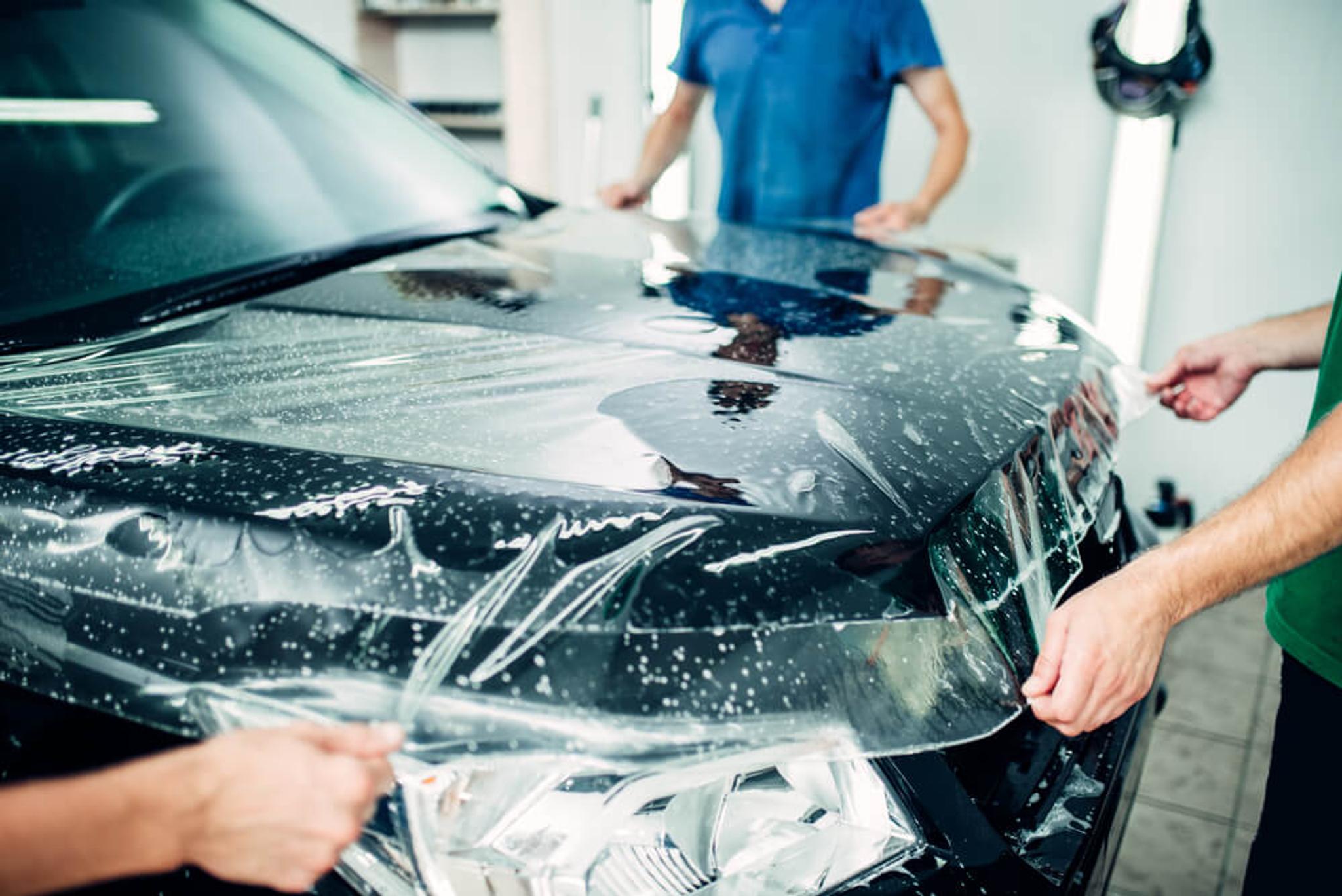 Three people apply paint protection film on a frontal part of black car