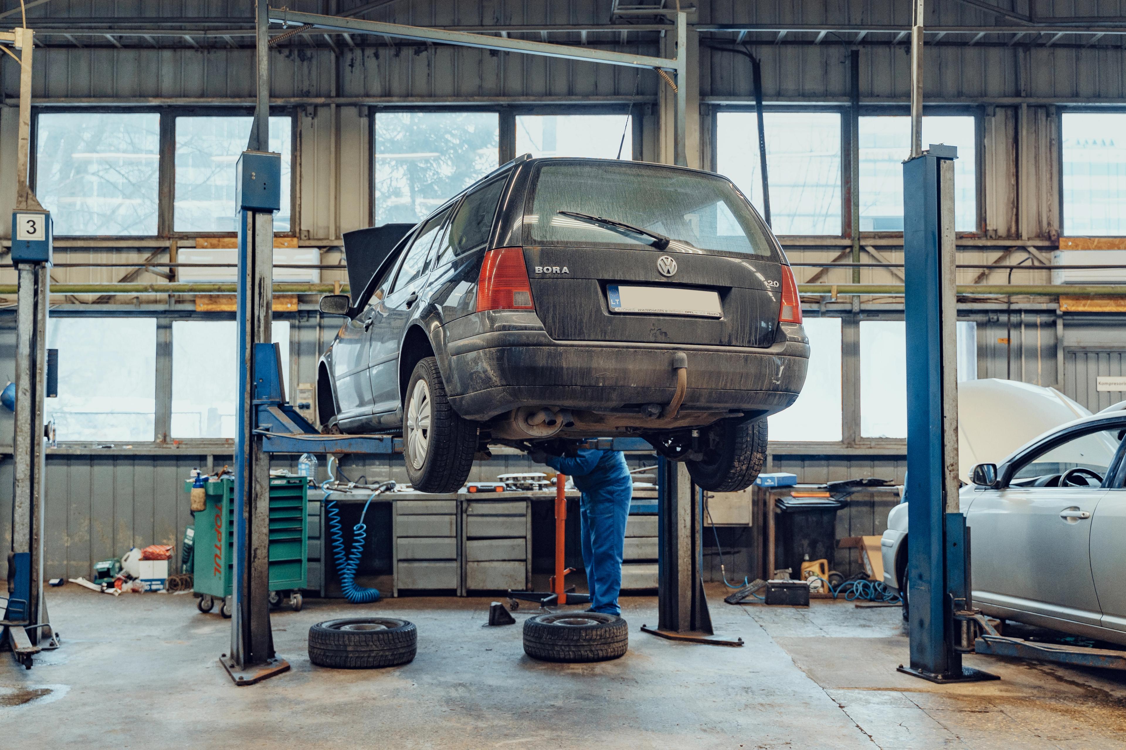 Mécanicien en train d'inspecter le dessous d'une voiture soulevée sur un pont élévateur dans un garage professionnel.
