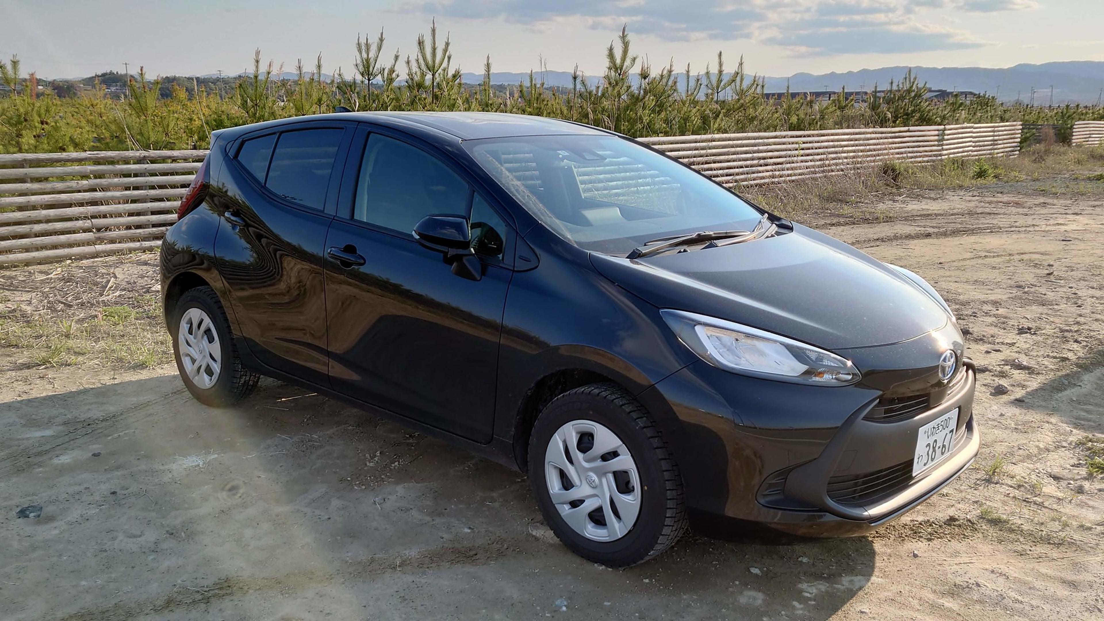 A black Toyota Aqua parked near the fence