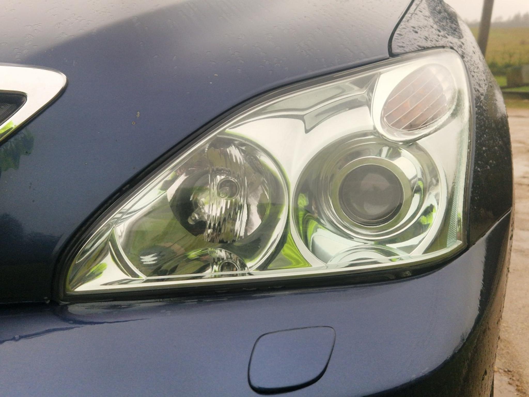 Un far stânga al unui Lexus în ploaie, cu mecanismul de spălat al farului vizibil