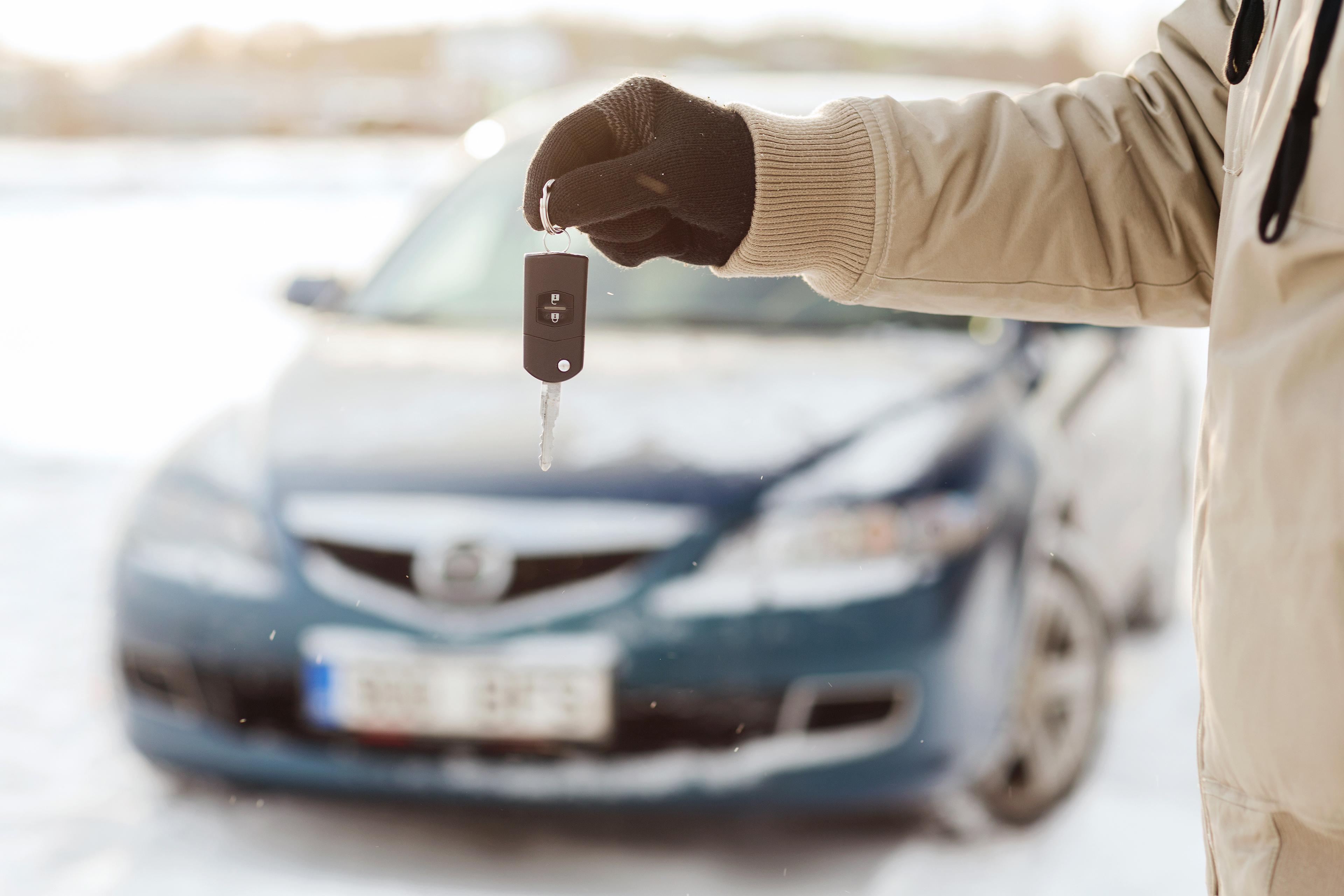 Man holding keys in front of a blue car