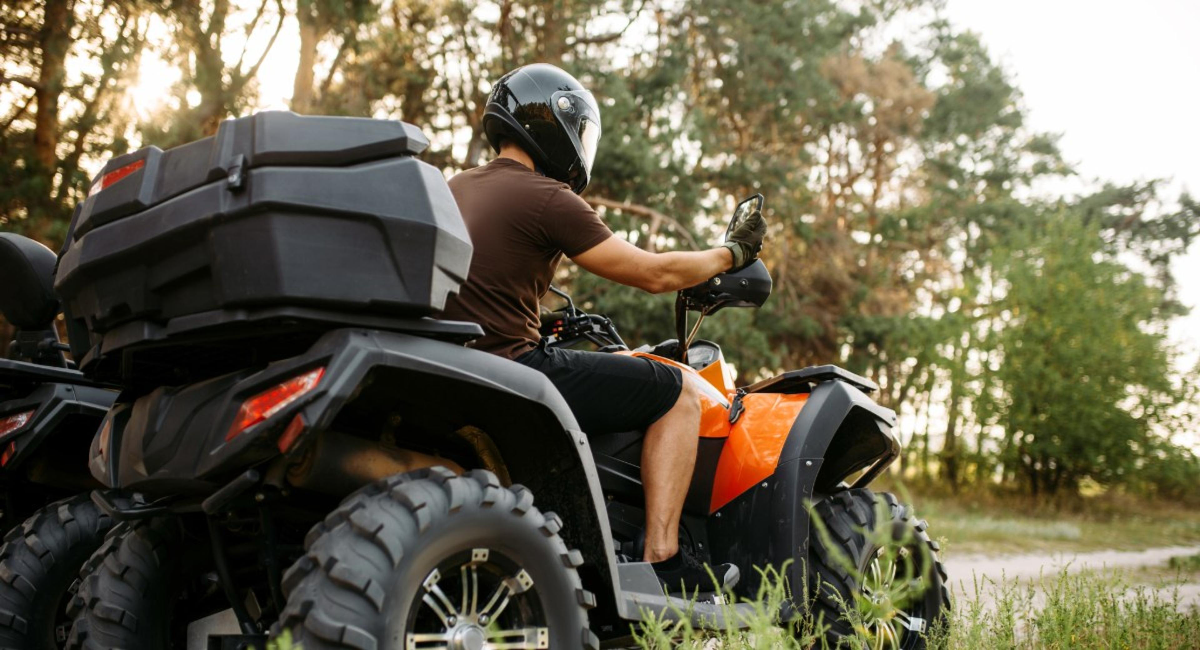 ATV rider wearing safety gear and helmet on orange all-terrain vehicle with cargo storage, showing importance of comprehensive ATV insurance protection